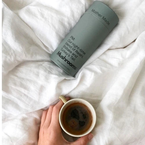 Mother Made mushroom powder container on a soft white linen background, paired with a cup of warm coffee. A natural, adaptogenic blend to support immunity, brain function, and overall well-being.