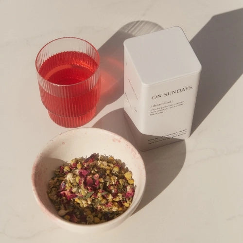 On Sundays Dreamland premium loose-leaf tea blend in a white box, displayed with a cup of vibrant On Sundays Mulled Wine brewed tea and a bowl of the Dreamland tea blend. 100% organic NZ made tea blends crafted for relaxation and wellness.