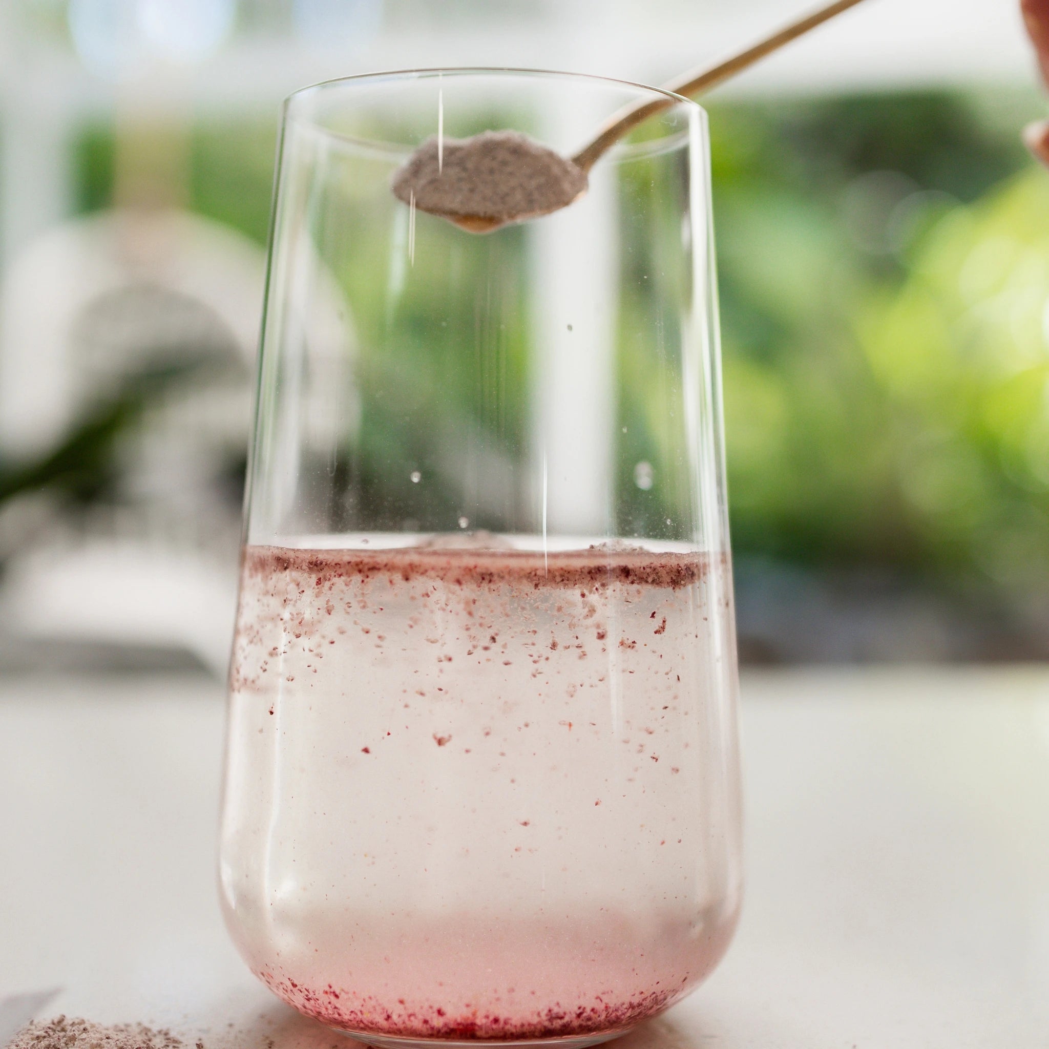 Vanessa Megan Astaxanthin and Marine Collagen Skin Boost powder being added to a glass of water, dissolving into a pink blend of natural collagen peptides, antioxidants and natural vitamin C.